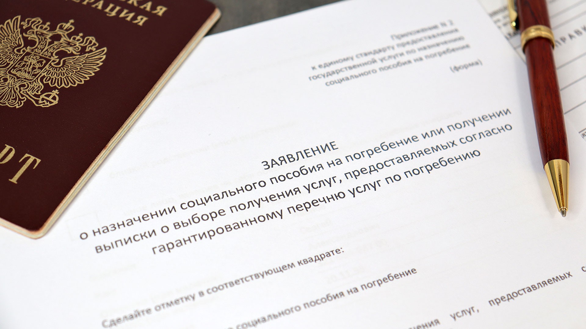 Бланк заявления на социальное пособие на погребение рядом с паспортом и ручкой